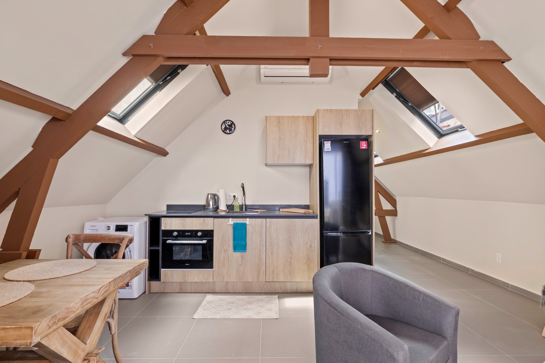The Loft: living and kitchen beneath restored timber roof trusses with yellow curtains